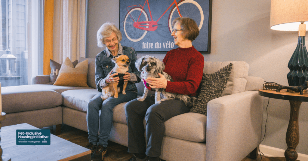 Two older women sitting on a couch each holding a small dog